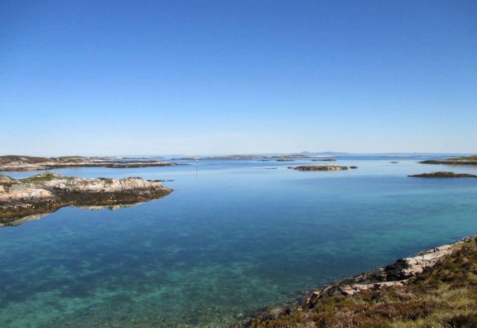 Utsikt over fjord eller innsjø, med noen få landbiter synlig til venste og i høyre hjørne, og videre ut i bakgrunnen. Skyfri himmel.