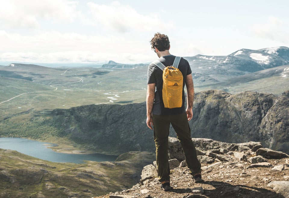 Person står med sekk på ryggen og ser utover vakkert fjellområde
