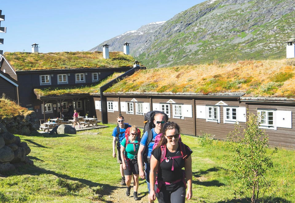 Turgjeng går vekk fra hytte med sekk på ryggen.