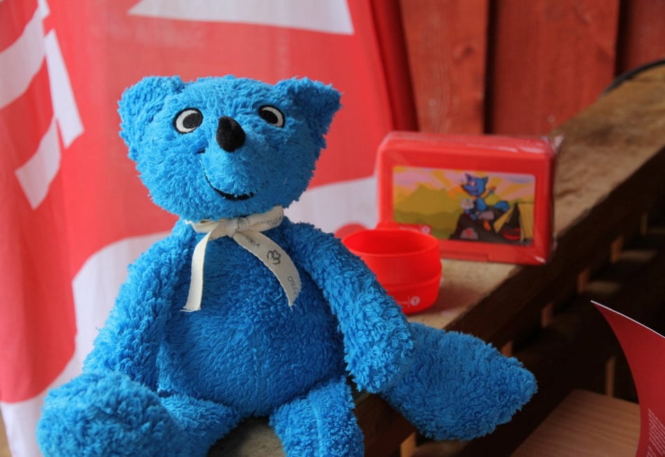 Kosedyr av masoten Turbo sitter på en vedskranke, med rødmalte vegger i bakgrunnen.