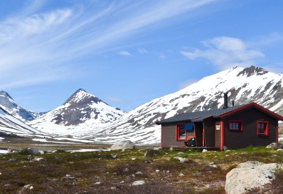 To hytter i sommerfjellet, snødekte fjell i bakgrunnen