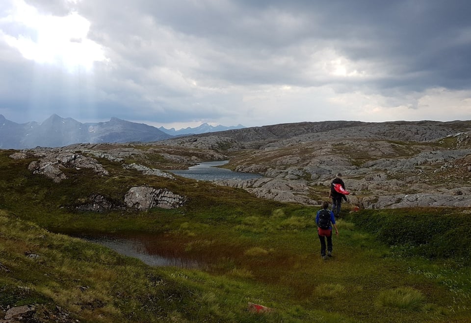 To turgåere går over svabergområde. Flotte fjell i bakgrunnen.