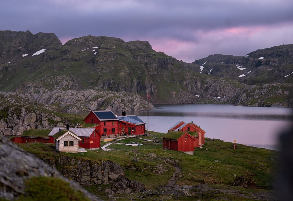 Røde hytter som ligger fint til ved et vann på fjellet.