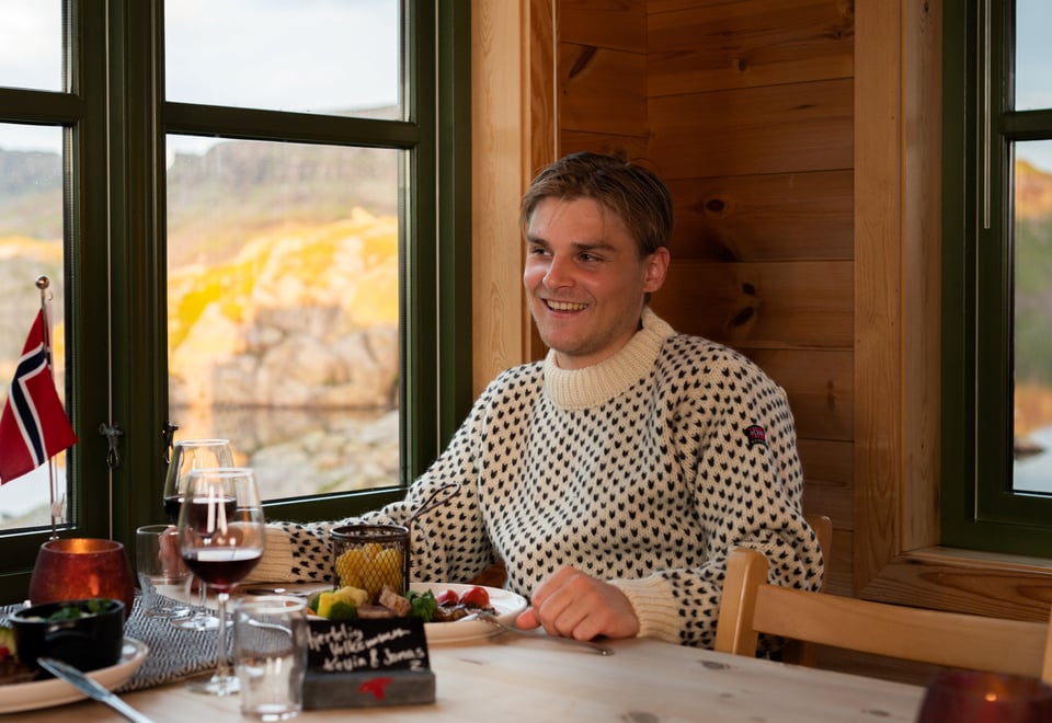 Bilde av en mann som sitter ved bordet og smiler. Bordet er dekket med flagg og servise.