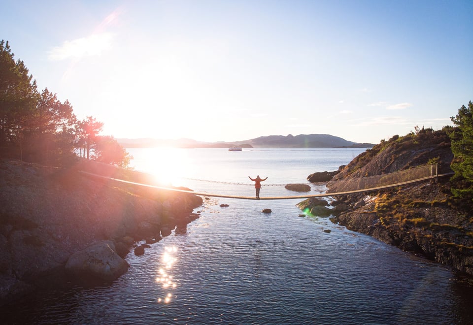 Dronebilde av hengebru på Vassøy i Stavanger. En person står i midten av broen og strekker armene ut.