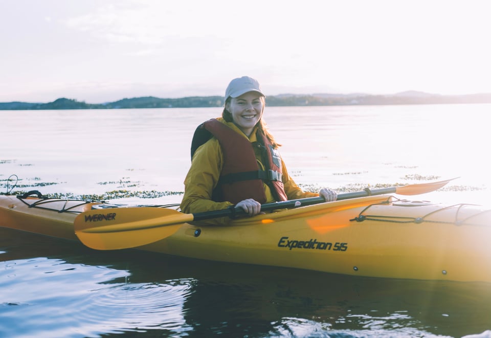 Kvinne som padler kajakk i solnedgang. Foto.