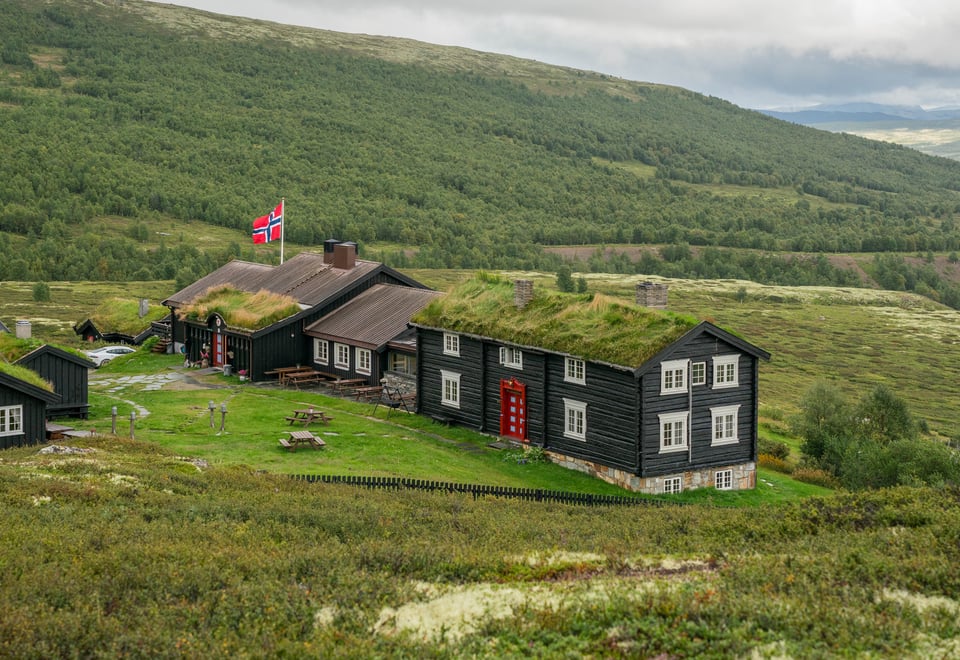 Svartmalt hytte med torv på taket og grønt gress rundt.