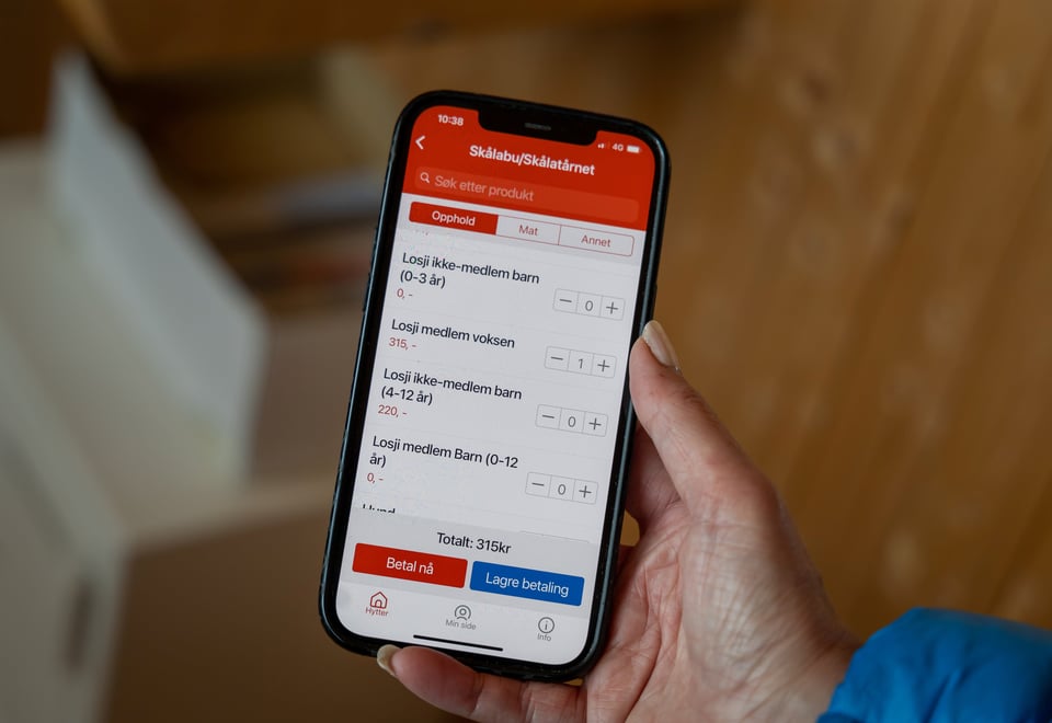 Mobiltelefon i hånden med ulike hyttekategorier.