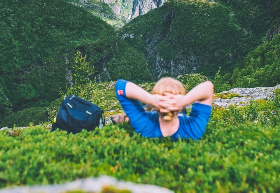 Mann som ligger i grønn lyng og ser utover fjell