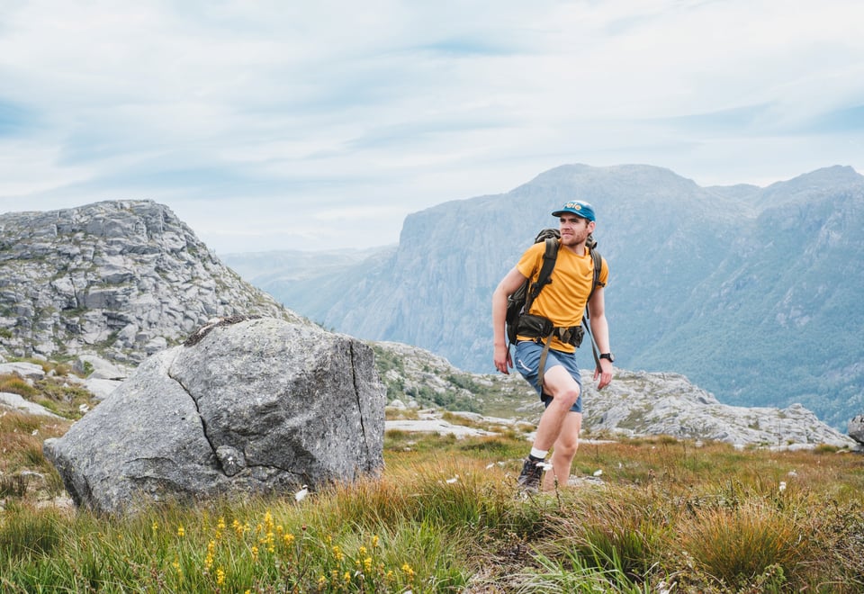 En mann i gul t-skjorte og shorts går på toppen av et fjell.