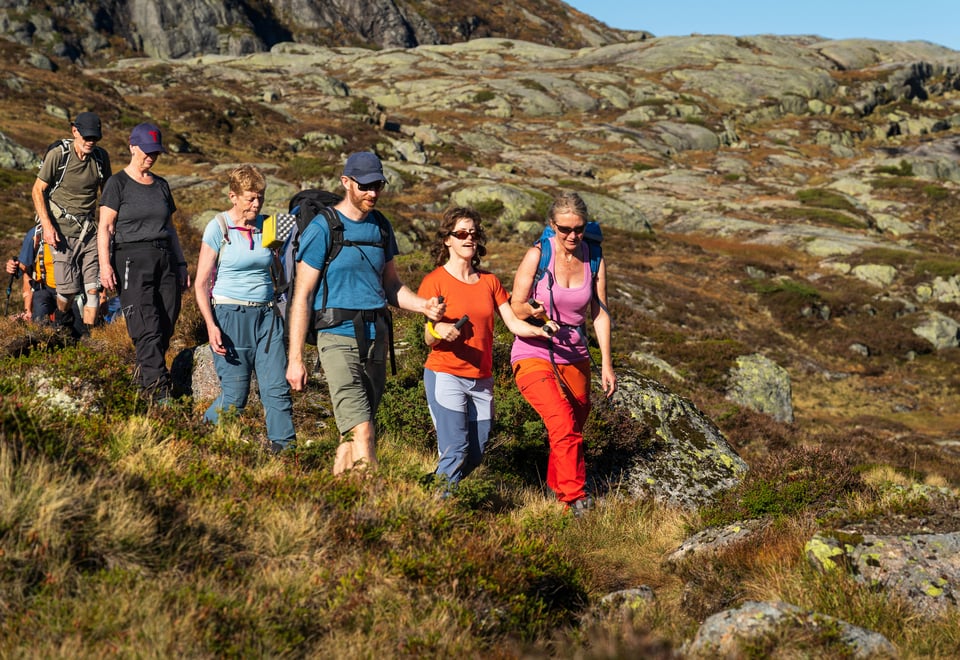 En gruppe mennesker går nedover en fjellside. Kvinnen som går i front blir støttet av ledsagere.