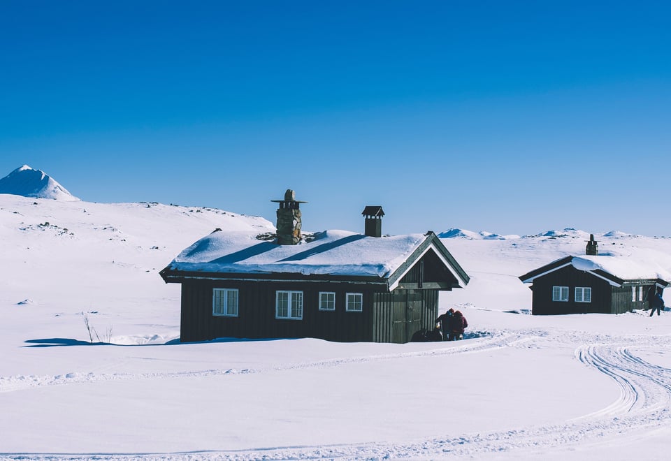 To svartmalte hytter i vinterlandskap og blå himmel