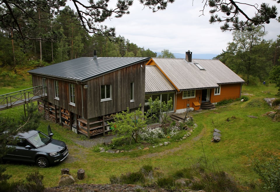 Okerfarget og grå, stor hytte som ligger ved skog og stor plen.