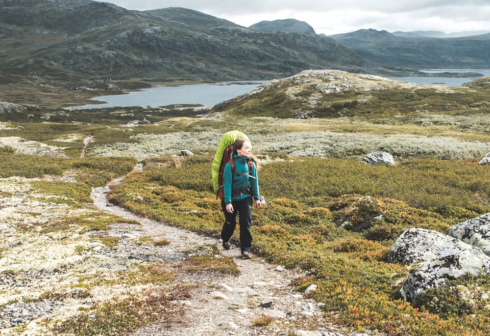 Dame med sekk på ryggen som går i fjellet