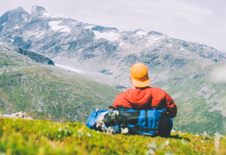 Mann med caps og rød jakke som ser utover fjellet.
