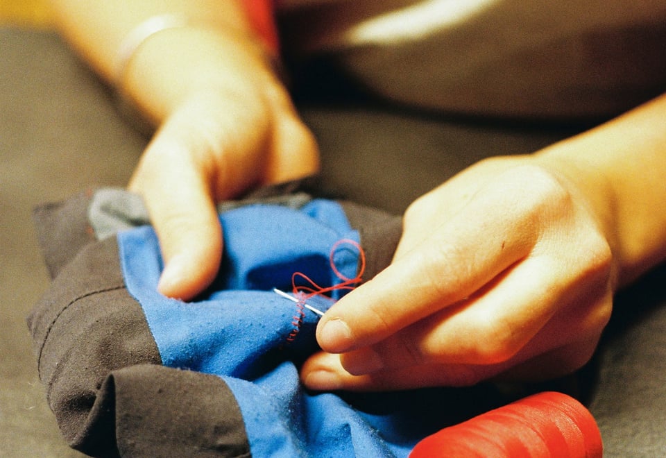 hender som syr blått stoff med rød tråd