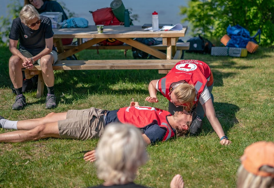 Person som ligger på bakken. Førstehjelp utøves.
