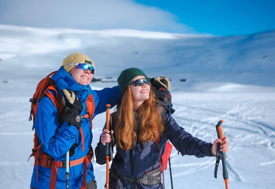 To kvinner med sekk på ryggen på ski i vinterlandskap