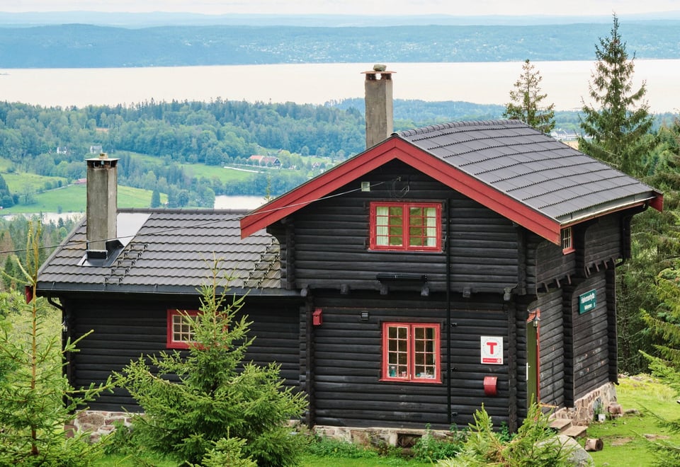 Svartmalt hytte med røde karmer med utsikt mot en fjord
