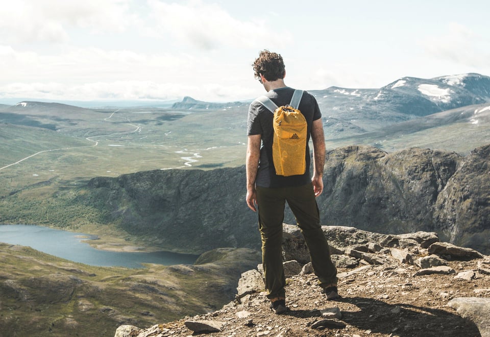 Mann med gul sekk som står på en fjellkant