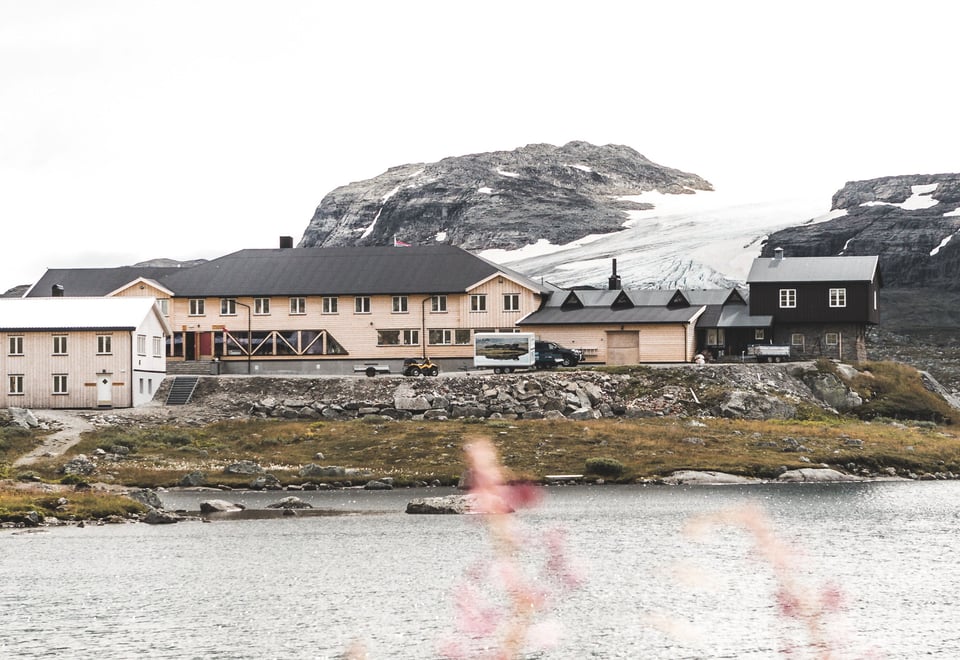 To svartmalte hytter med vann og blomster i forgrunnen