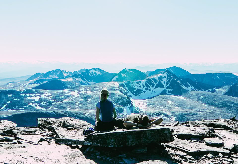 To personer som ligger på en stein og ser utover et fjellområde