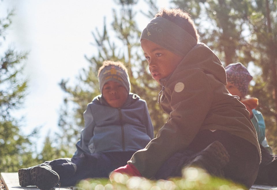 Tre barn som sitter på bakken i skogen
