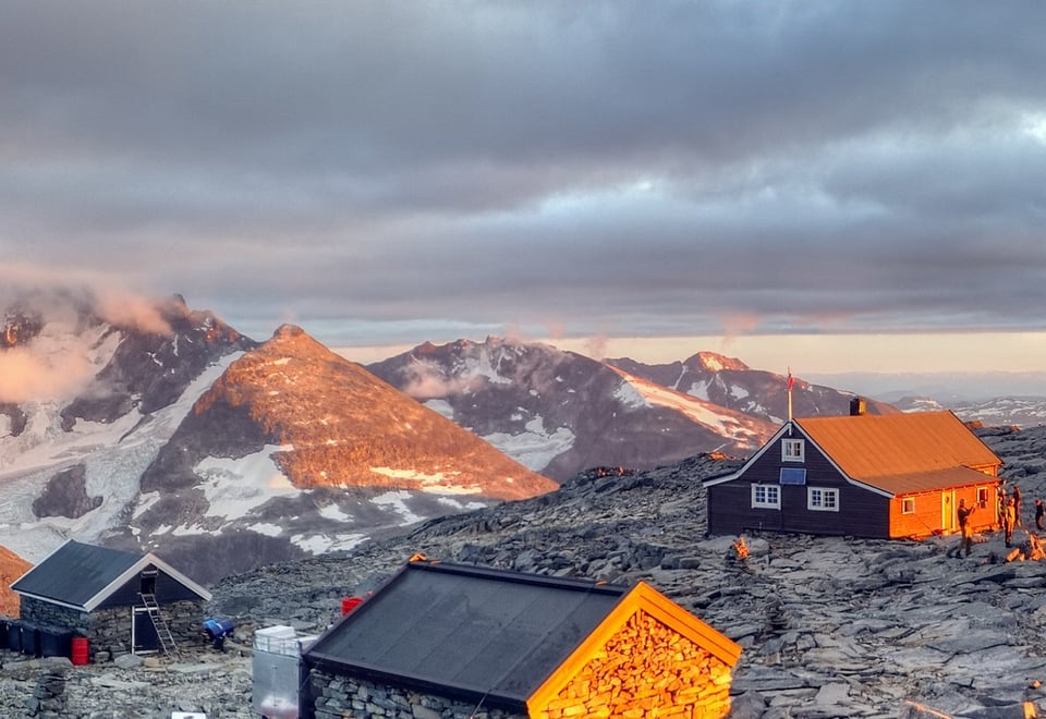 Solnedgang og liv på Fannaråkhytta. Hurrungane sees i bakgrunnen, mens Lusterfjorden kan skimtes til høyre.  [vegard.r.stenerud@gmail.com, 48007757] DNTs Fotokonkurranse- DNT hytteliv. Vår 20123. plass