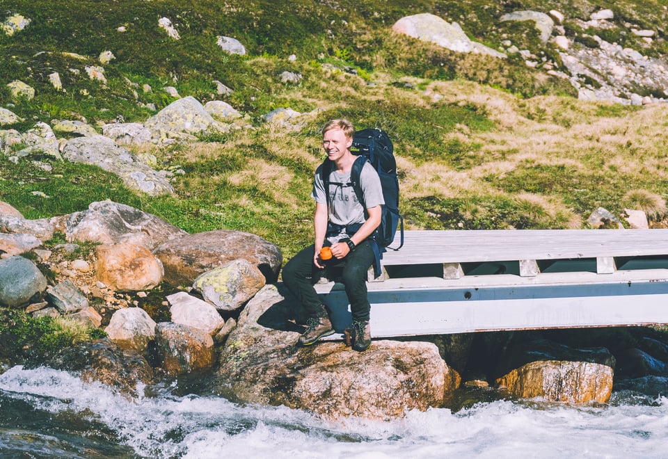 En person som sitter på en bro ved en elv i fjellet