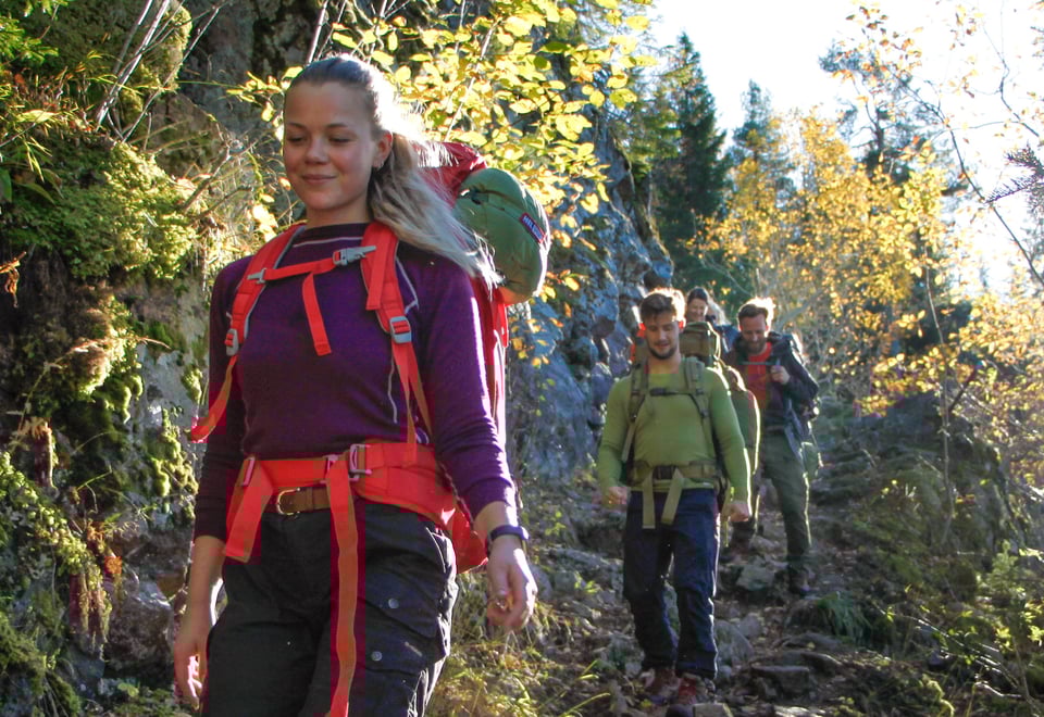 Personer med sekk som går på en sti i skogen