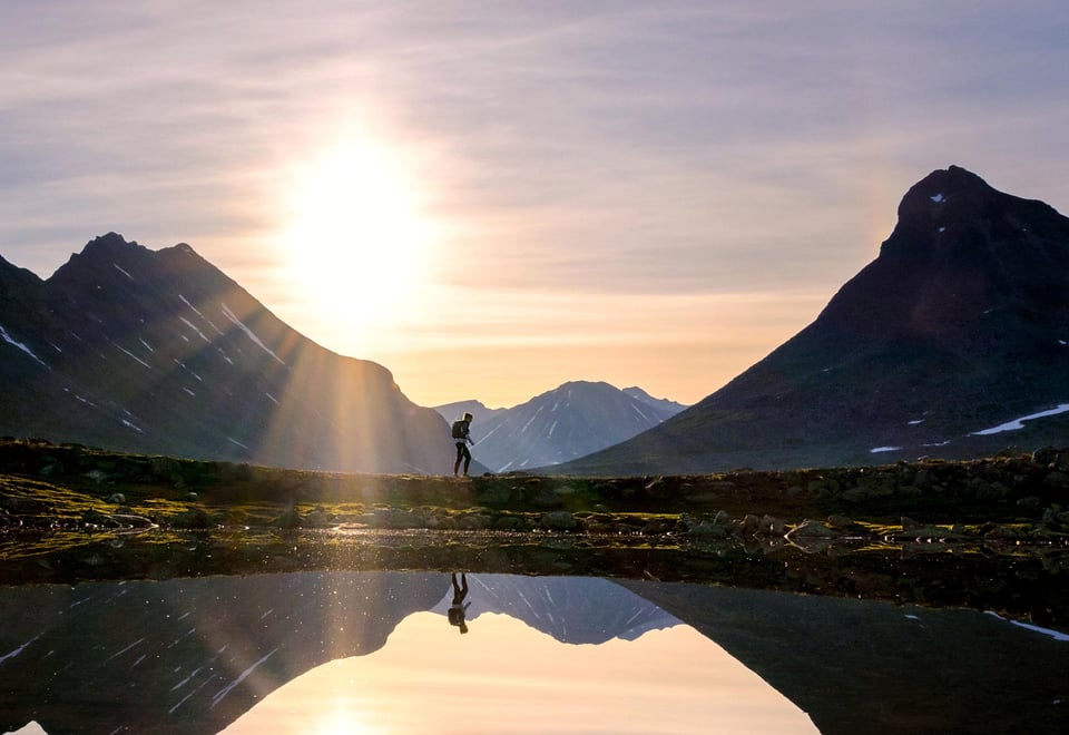 Person som går i fjellet med solnedgang i bakgrunnen
