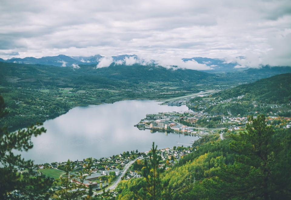 En innsjø med fjell i bakgrunnen og grønn skog rundt