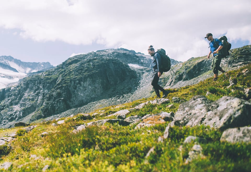 To menn går i flott fjellandskap. Sommer.