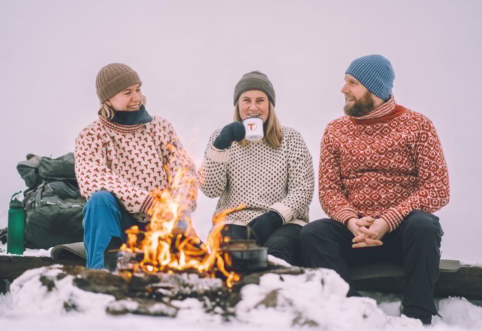 Tre mennesker sitter ved bål og smiler.