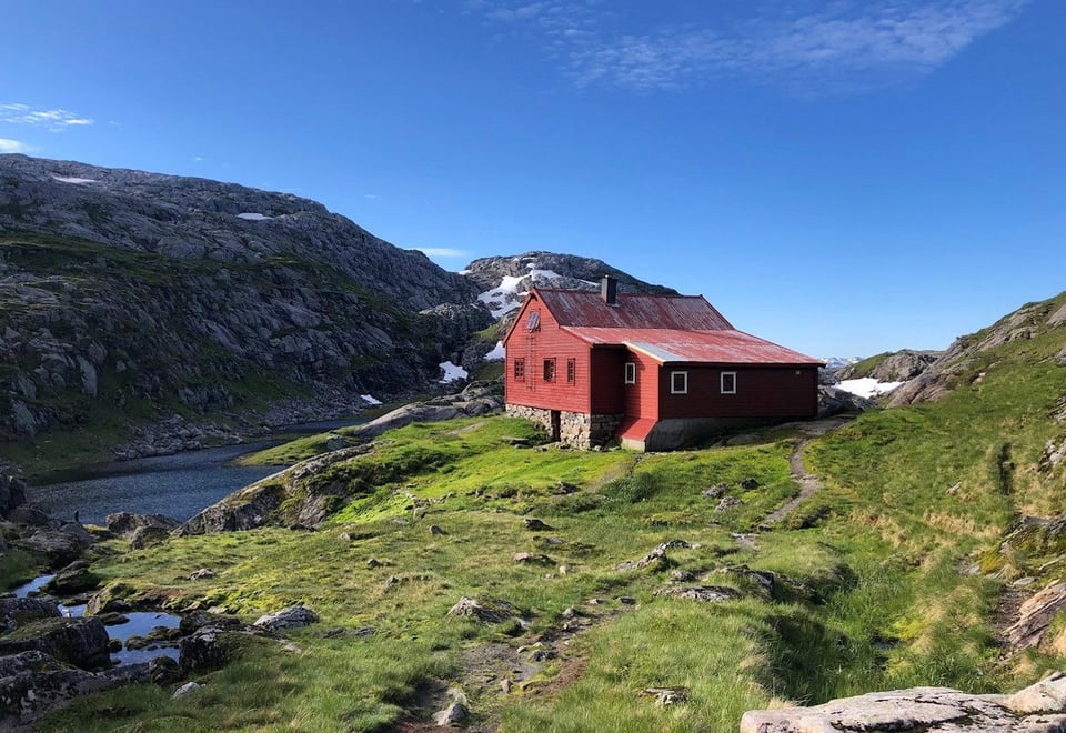 Rødmalt hytte med slitt tak omkranset av fjell.