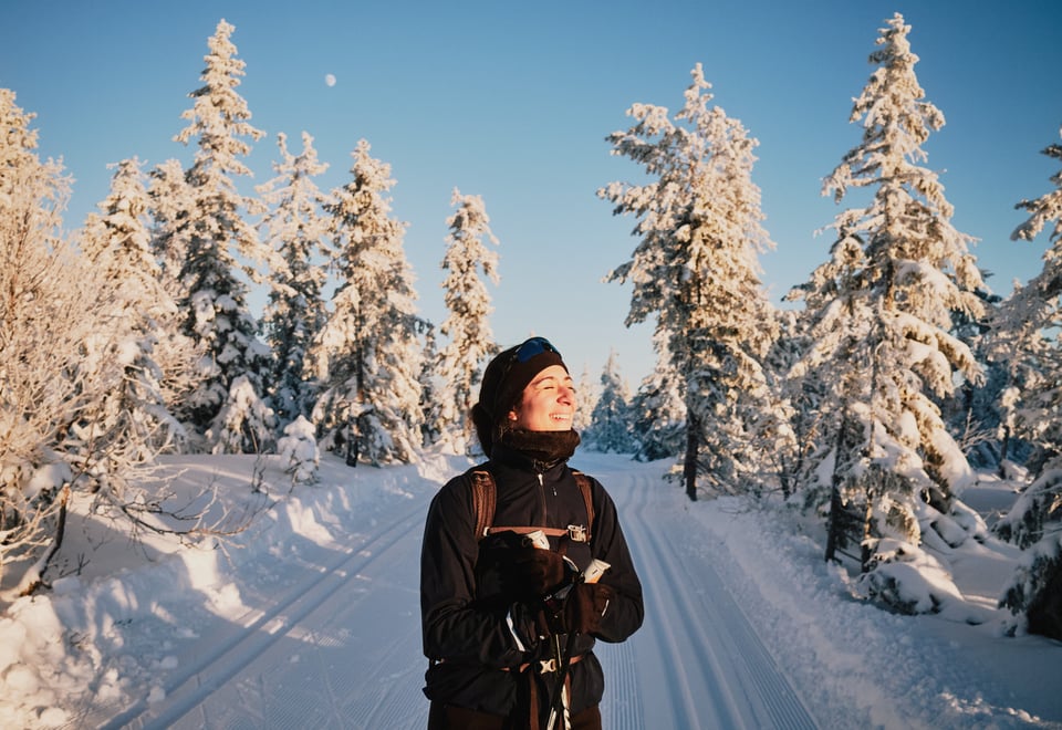 Smilende kvinne på ski i snødekt skog.