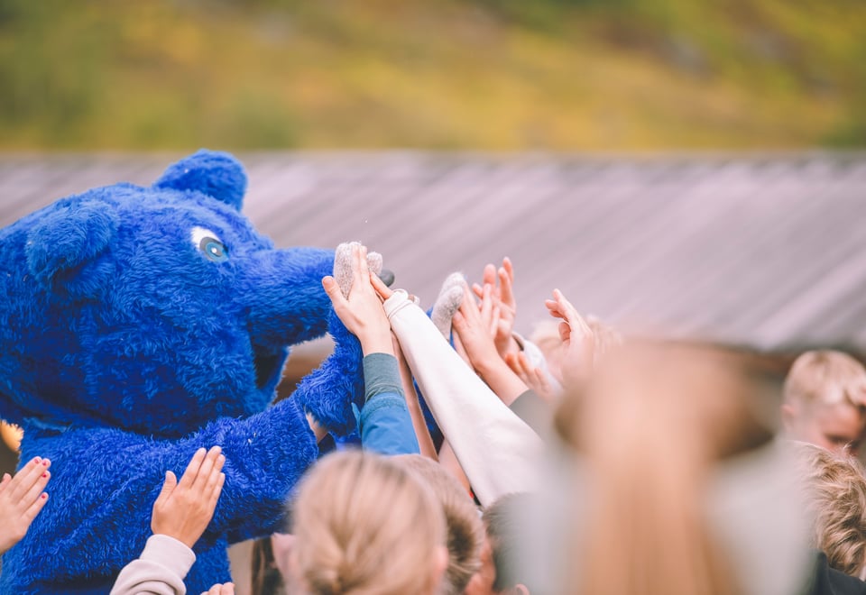 Turbo, en blå maskot gir high five til flere barn.