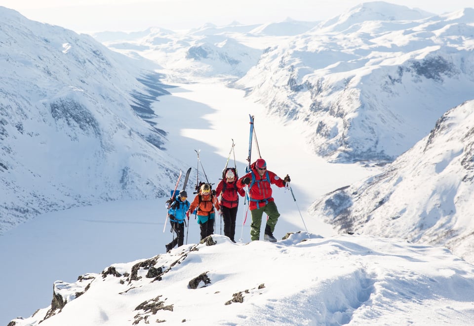 En rekke personer som går på et vinterkledd fjell.