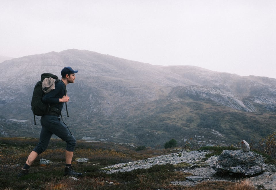 Mann går på tur foran skoddekledd fjell.
