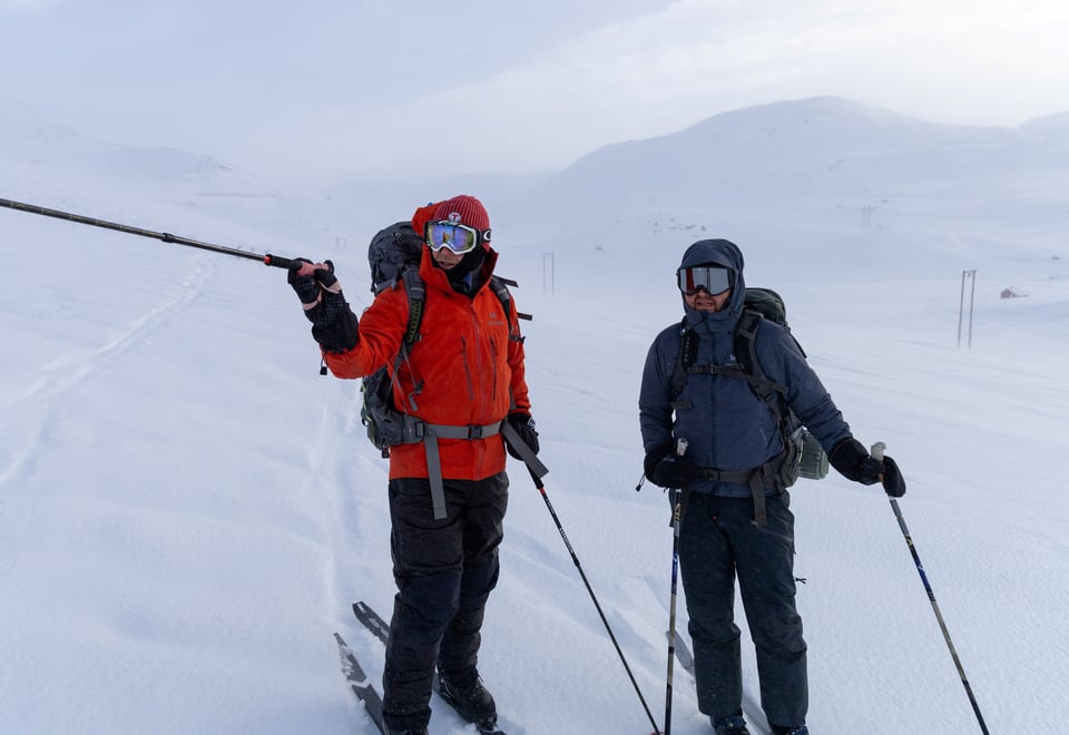 To vinterkledde menn med fullt vintertøy står ute på ski i fjellet.