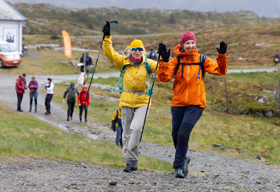 To kvinner jubler og løfter hendene i været. De går på grusvei med mange folk bak.