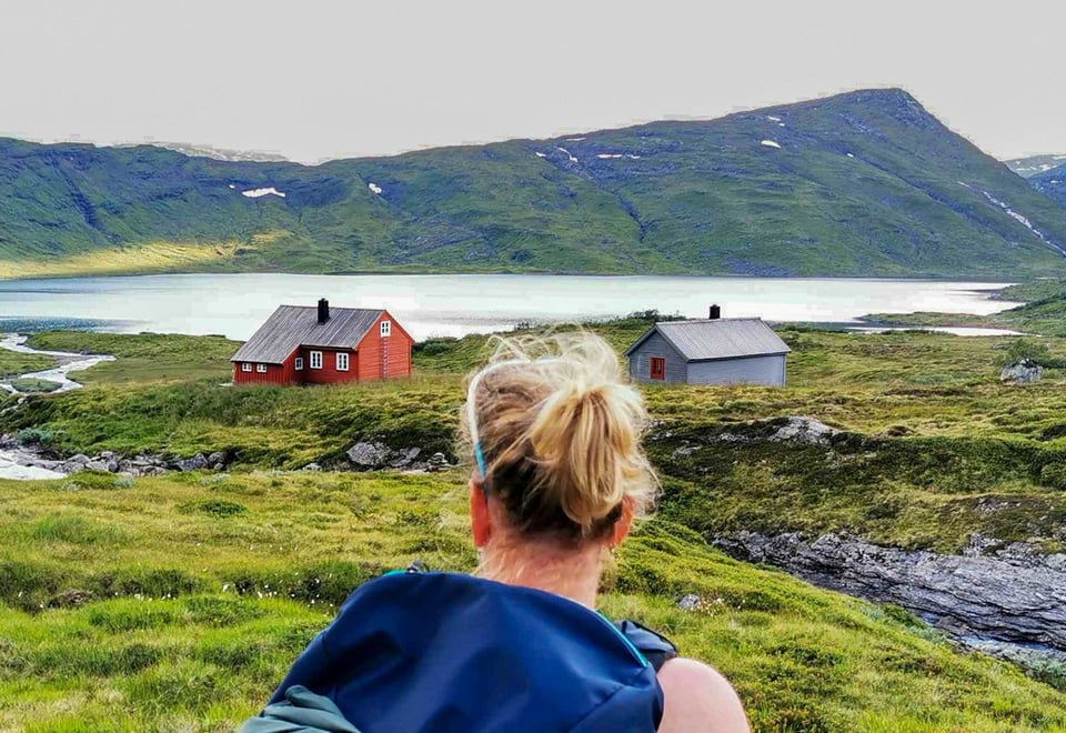 Kvinne med ryggen til kamera ser mot en hytte i det fjerne.