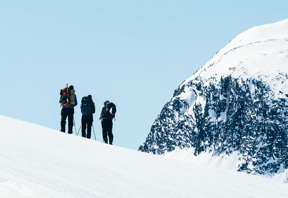 Tre personer med skiutstyr som står på en fjelltopp