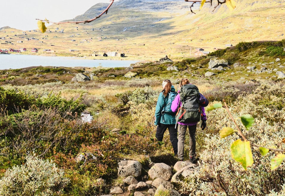 To personer med sekk som går på en sti i grønt fjellterreng