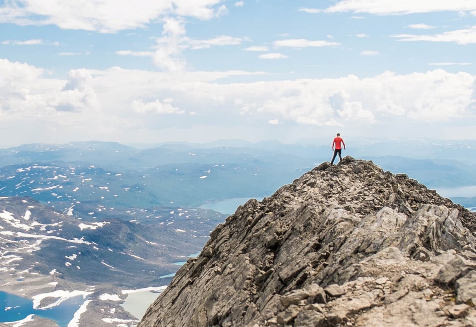 Mann som står på toppen av en fjelltopp og ser utover. 
