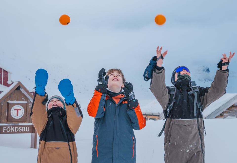 Tre barn som kaster appelsin opp i luften. Det er vinter