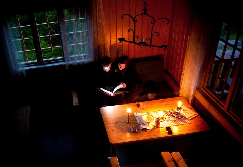 To personer som sitter ved et bord med levende lys og hodelykt og leser.