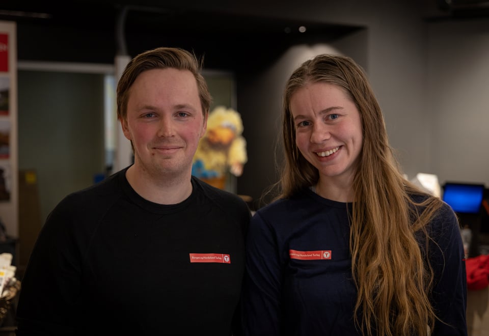 Mann og kvinne i T-merket genser smiler til kamera innendørs.