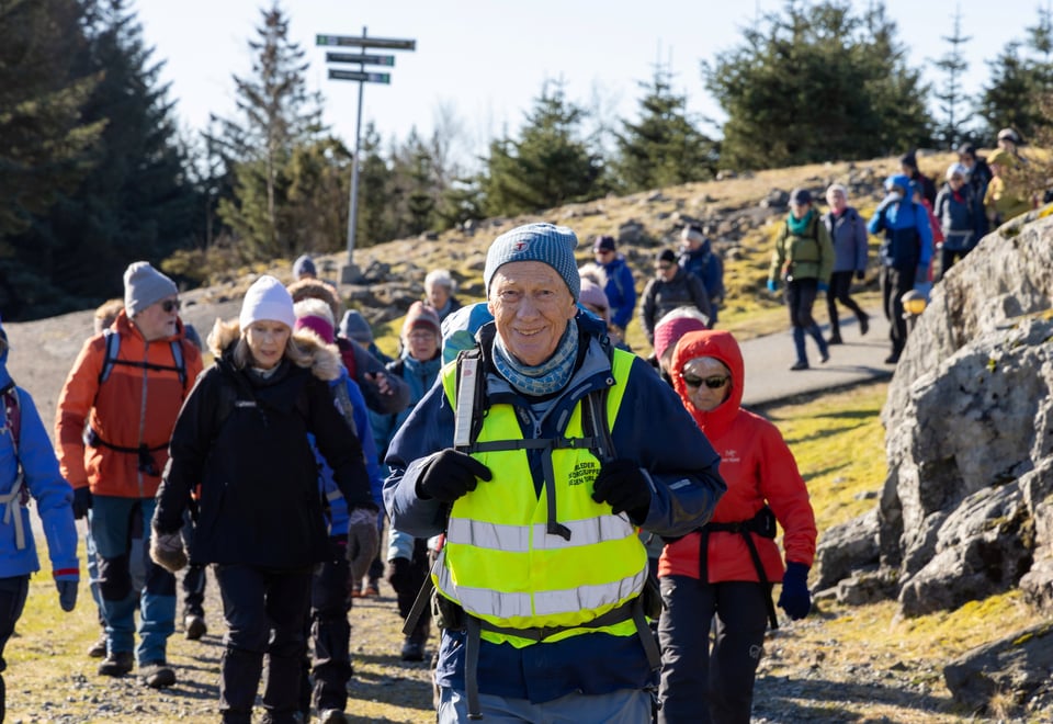 Senior turleder på tur i gul refleksvest med flere turgåere bak seg.