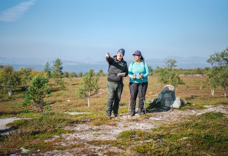 To personer som ser dit mannen peker. De står i et fjellområde, det er blå himmel